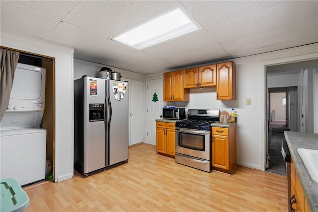 kitchen with a drop ceiling, stainless steel appliances, stacked washer and clothes dryer, and light wood-type flooring