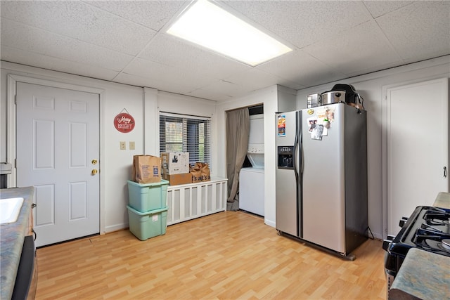 kitchen featuring black range with gas stovetop, stainless steel fridge, light wood-type flooring, and stacked washer and dryer