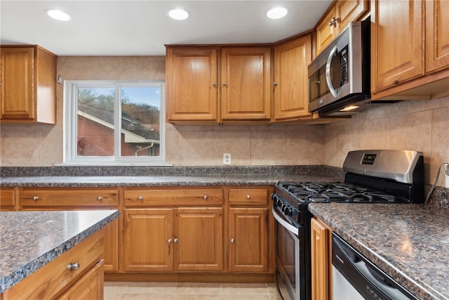 kitchen featuring appliances with stainless steel finishes, light tile patterned floors, and dark stone countertops