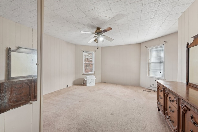 spare room featuring light carpet, ceiling fan, and wooden walls