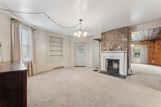 unfurnished living room featuring built in shelves, light colored carpet, a notable chandelier, a fireplace, and wood walls