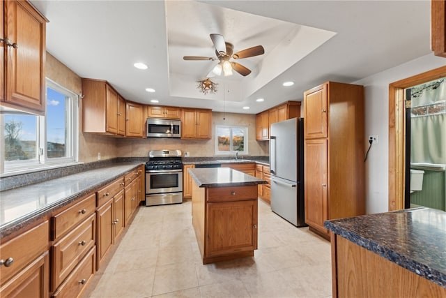 kitchen with ceiling fan, a center island, stainless steel appliances, a raised ceiling, and light tile patterned floors