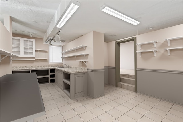 kitchen with light tile patterned flooring, a textured ceiling, gray cabinets, and sink