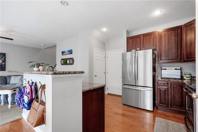 kitchen with black / electric stove, stainless steel fridge, stone counters, and wood-type flooring