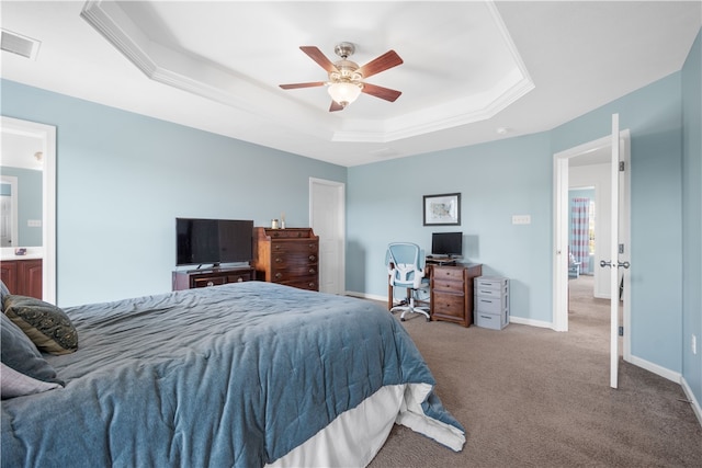 bedroom featuring light carpet, ensuite bathroom, ceiling fan, and a tray ceiling