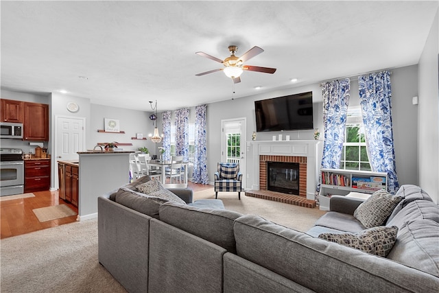 living room with a fireplace, light hardwood / wood-style floors, and ceiling fan with notable chandelier