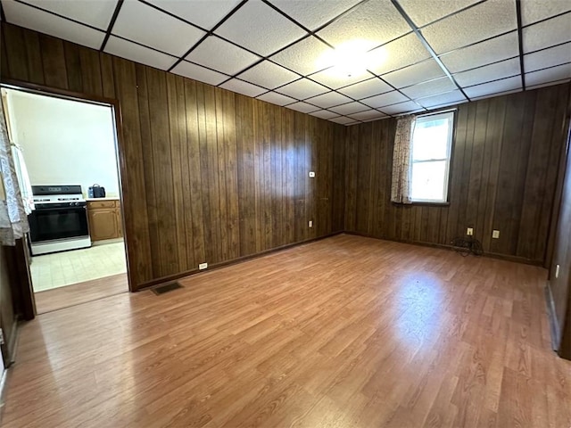 empty room featuring a paneled ceiling, wood walls, and light wood-type flooring