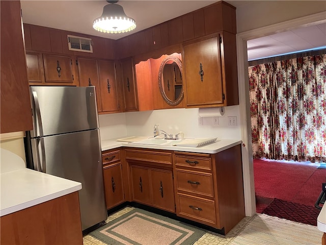 kitchen with decorative light fixtures, stainless steel refrigerator, and sink