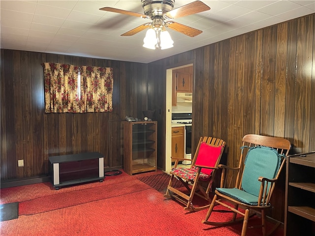 sitting room with carpet flooring, ceiling fan, and wood walls