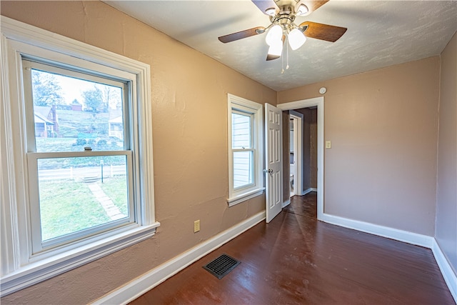 empty room featuring a wealth of natural light, ceiling fan, and dark hardwood / wood-style floors