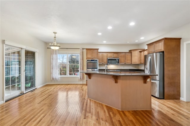 kitchen featuring pendant lighting, a kitchen island with sink, a breakfast bar area, light hardwood / wood-style floors, and stainless steel appliances