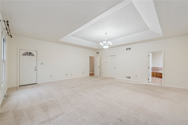 carpeted empty room featuring a raised ceiling and a chandelier