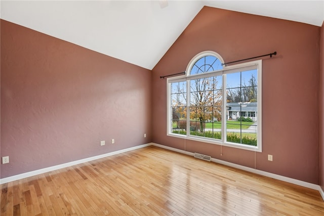 spare room with high vaulted ceiling and light wood-type flooring