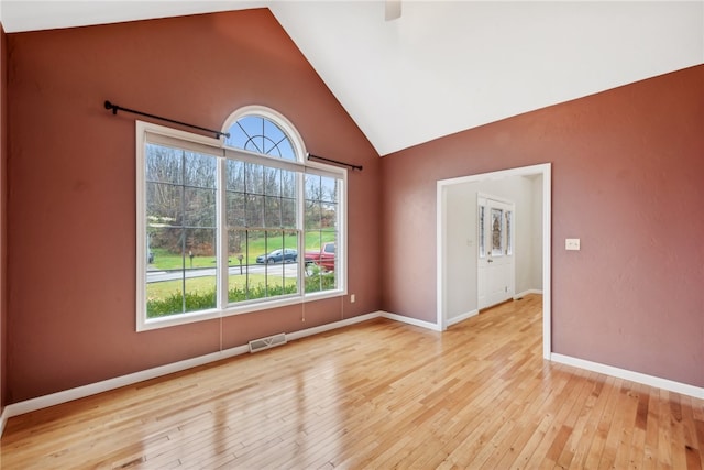 empty room with high vaulted ceiling, light hardwood / wood-style flooring, and a wealth of natural light