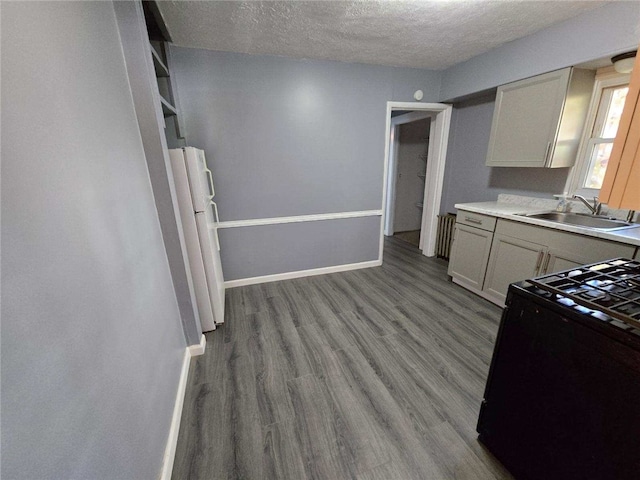 kitchen with a textured ceiling, sink, black range, white fridge, and light hardwood / wood-style floors