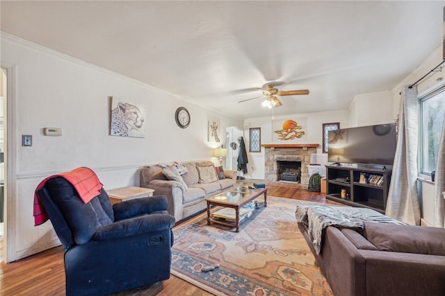 living room featuring ceiling fan, crown molding, wood-type flooring, and a fireplace