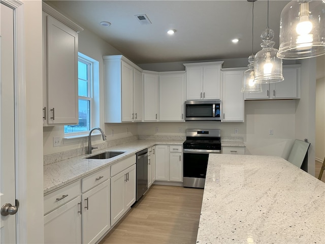 kitchen featuring sink, white cabinetry, hanging light fixtures, stainless steel appliances, and light stone counters