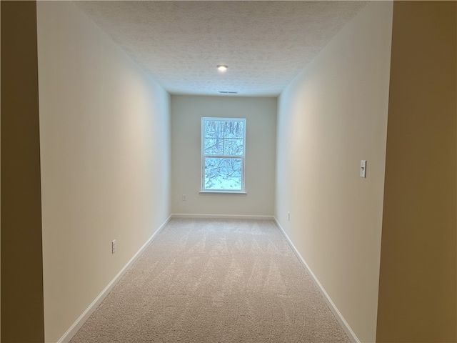 hallway with light colored carpet and a textured ceiling