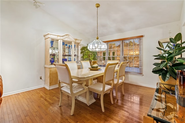 dining space with wood-type flooring, lofted ceiling, and an inviting chandelier