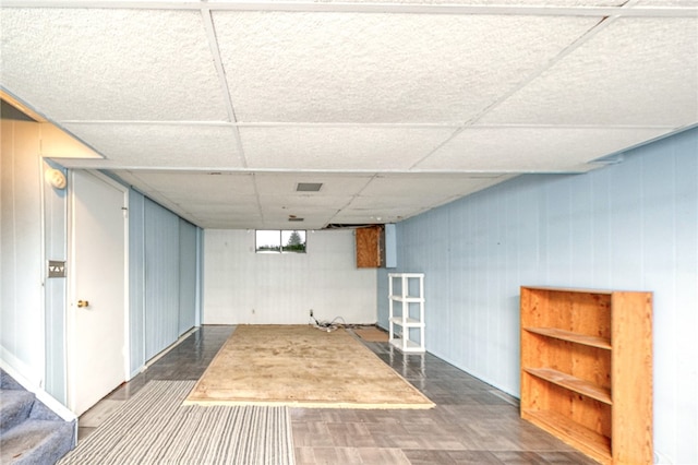 basement with a paneled ceiling and wooden walls