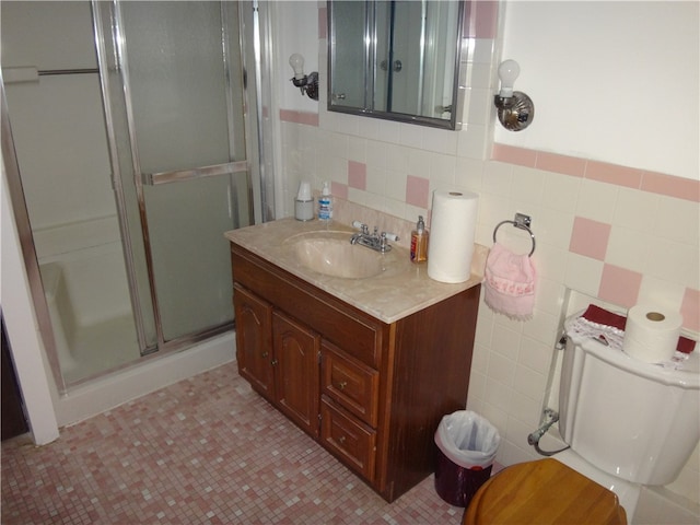 bathroom featuring tile patterned floors, an enclosed shower, toilet, vanity, and tile walls