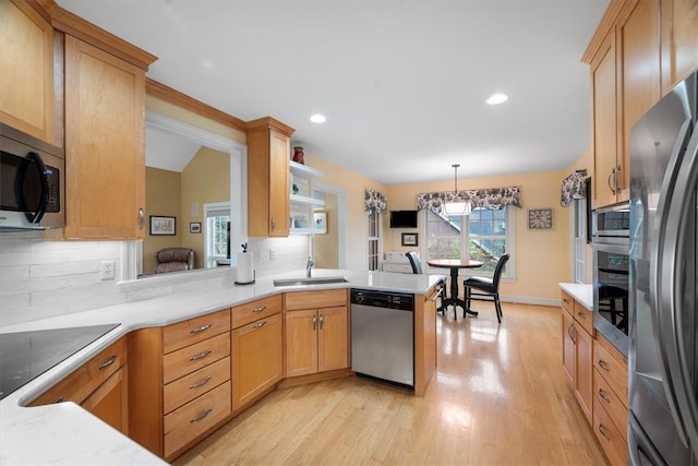 kitchen with sink, light wood-type flooring, appliances with stainless steel finishes, decorative light fixtures, and kitchen peninsula