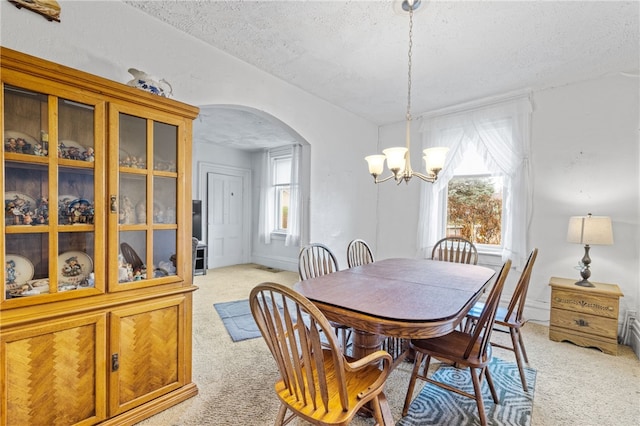 dining area with light carpet, a textured ceiling, and an inviting chandelier