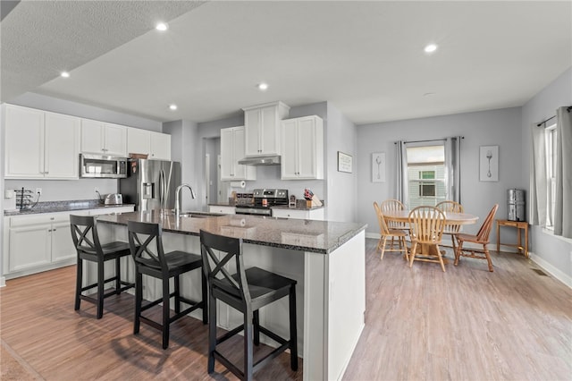 kitchen featuring a kitchen bar, a kitchen island with sink, white cabinets, and stainless steel appliances