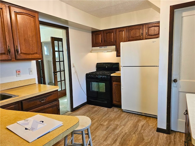 kitchen featuring white fridge, a textured ceiling, gas stove, and light wood-type flooring