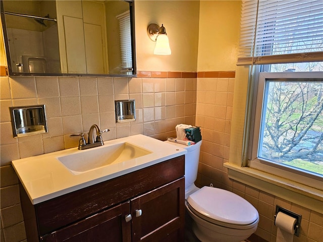 bathroom with toilet, vanity, tile walls, and plenty of natural light