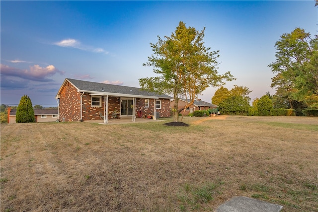 back house at dusk featuring a lawn and a patio area