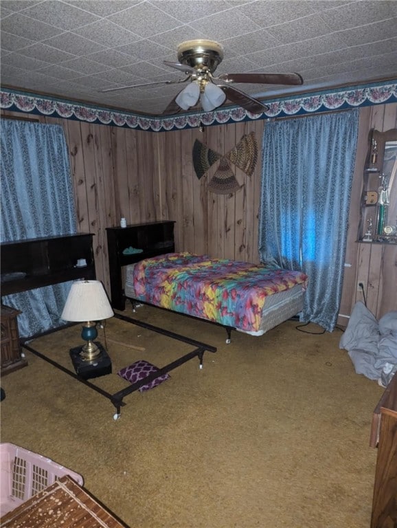 carpeted bedroom featuring ceiling fan and wooden walls