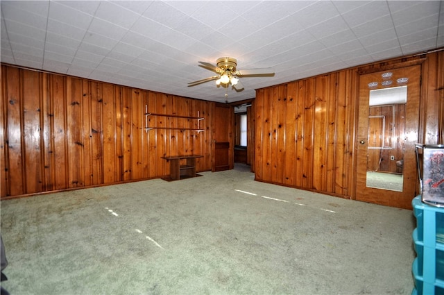 spare room featuring wood walls, ceiling fan, and light carpet