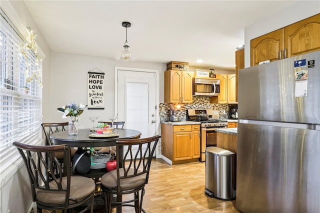 kitchen featuring hanging light fixtures, light stone countertops, tasteful backsplash, light hardwood / wood-style floors, and stainless steel appliances