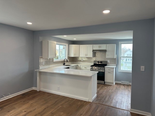 kitchen with kitchen peninsula, dark wood-type flooring, sink, stainless steel range oven, and white cabinetry