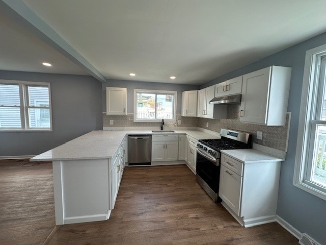 kitchen featuring kitchen peninsula, decorative backsplash, dark hardwood / wood-style flooring, stainless steel appliances, and white cabinetry