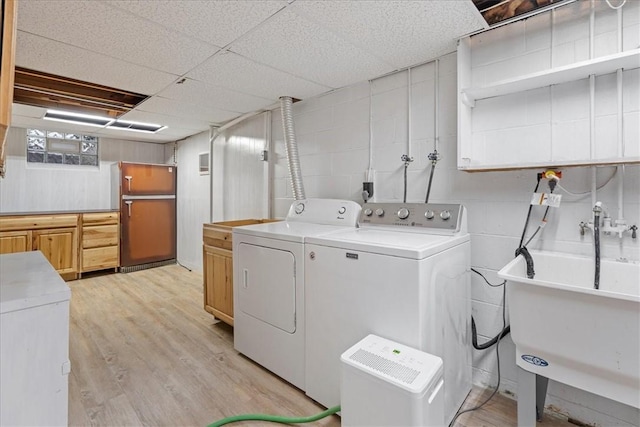 laundry area with cabinets, washer and clothes dryer, light hardwood / wood-style floors, and sink