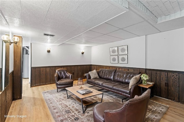 living room with a drop ceiling and light wood-type flooring