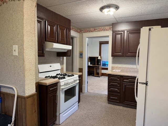 kitchen featuring wood walls, dark brown cabinets, light carpet, and white appliances