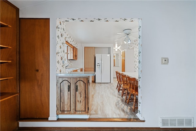 kitchen with ceiling fan, white fridge with ice dispenser, light hardwood / wood-style floors, and sink