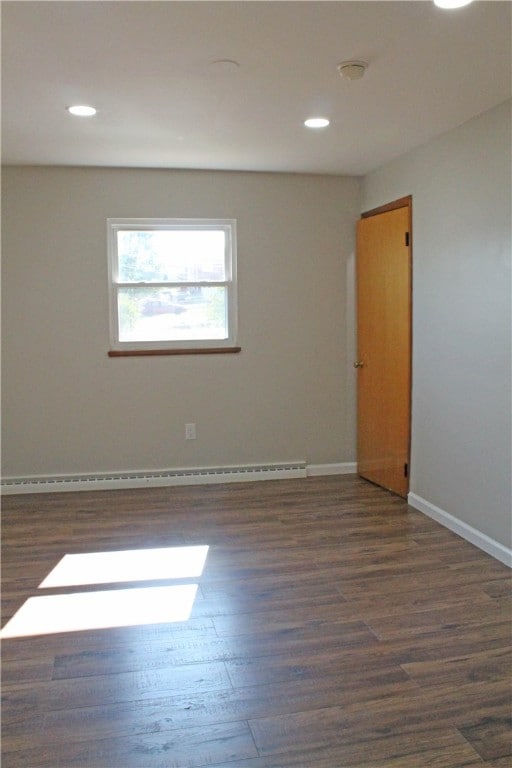 empty room with dark hardwood / wood-style floors and a baseboard heating unit