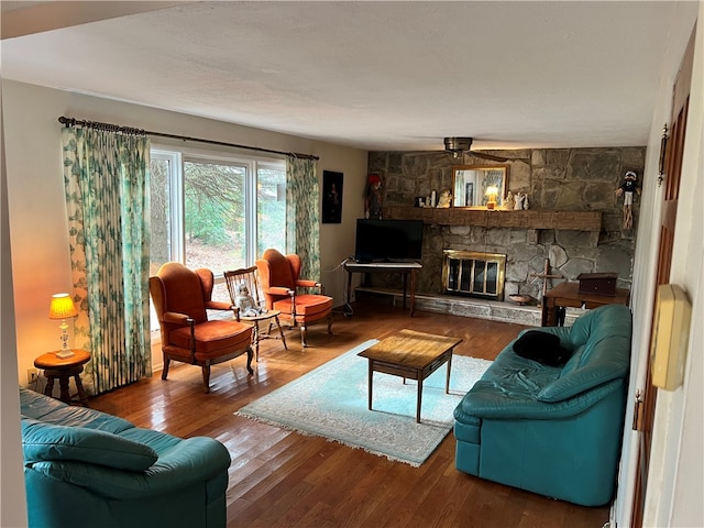 living room with wood-type flooring, a stone fireplace, and ceiling fan