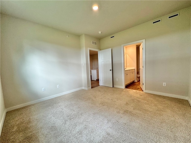 unfurnished bedroom featuring light carpet and ensuite bath