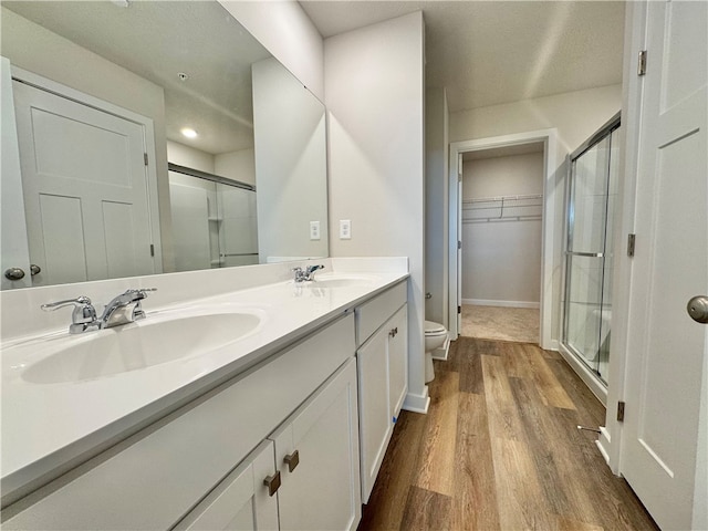 bathroom with hardwood / wood-style flooring, vanity, toilet, and a shower with door