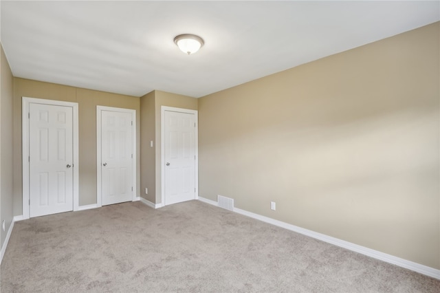 unfurnished bedroom featuring light colored carpet and multiple closets