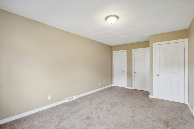 unfurnished bedroom featuring multiple closets and light carpet