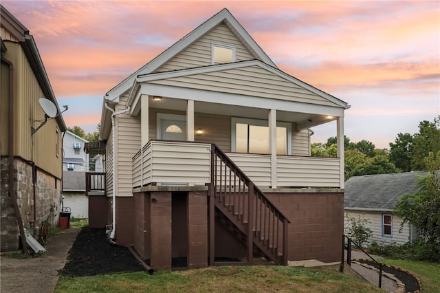 back house at dusk featuring covered porch