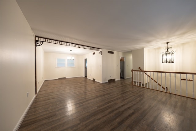 spare room with a notable chandelier and dark wood-type flooring