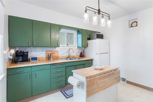 kitchen featuring decorative backsplash, sink, green cabinetry, white fridge, and hanging light fixtures