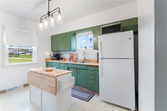 kitchen with decorative backsplash, sink, decorative light fixtures, green cabinetry, and white fridge